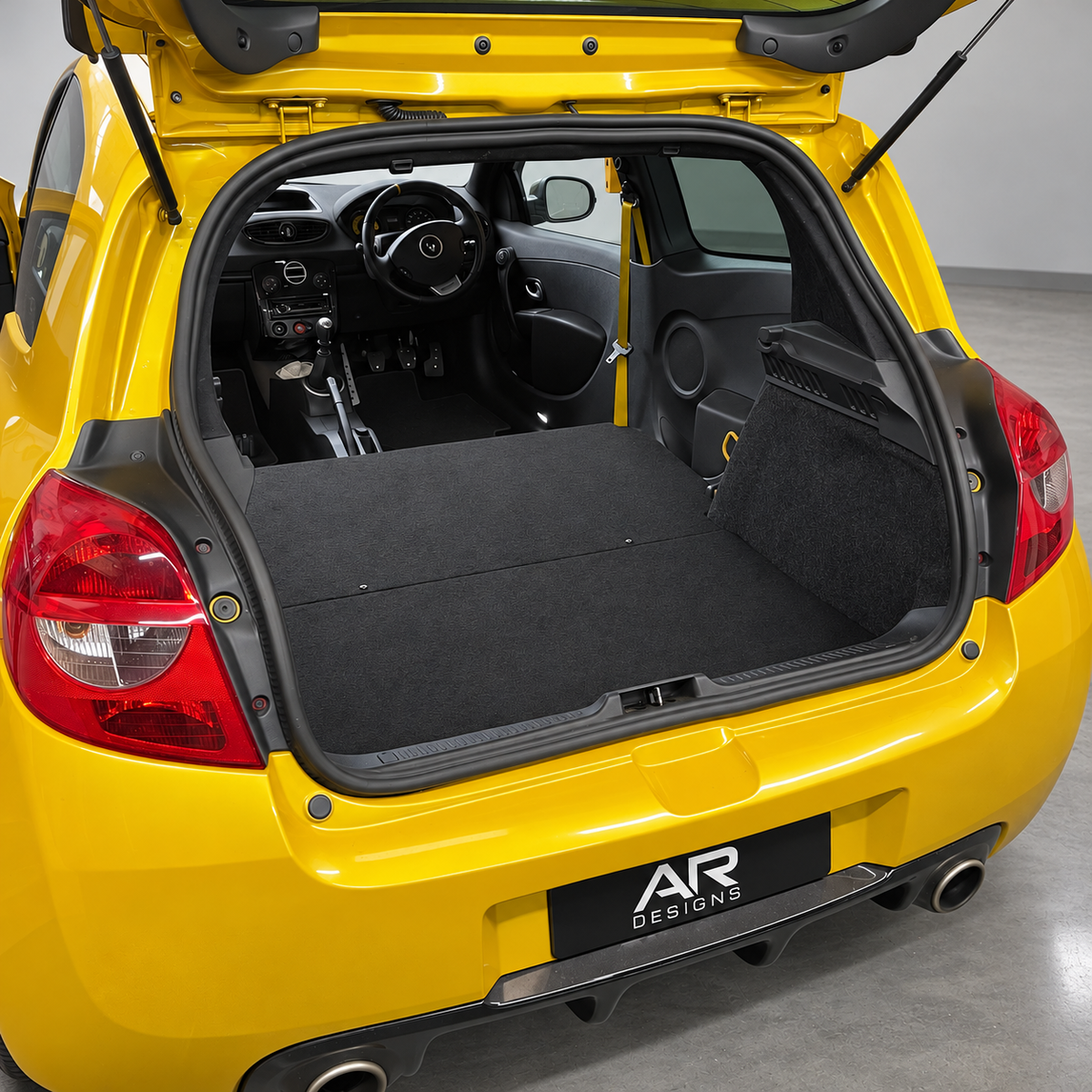 Black rear seat delete floor kit installed in a yellow Renault Clio, with an AR Designs numberplate cover; photograph retouched for presentation.